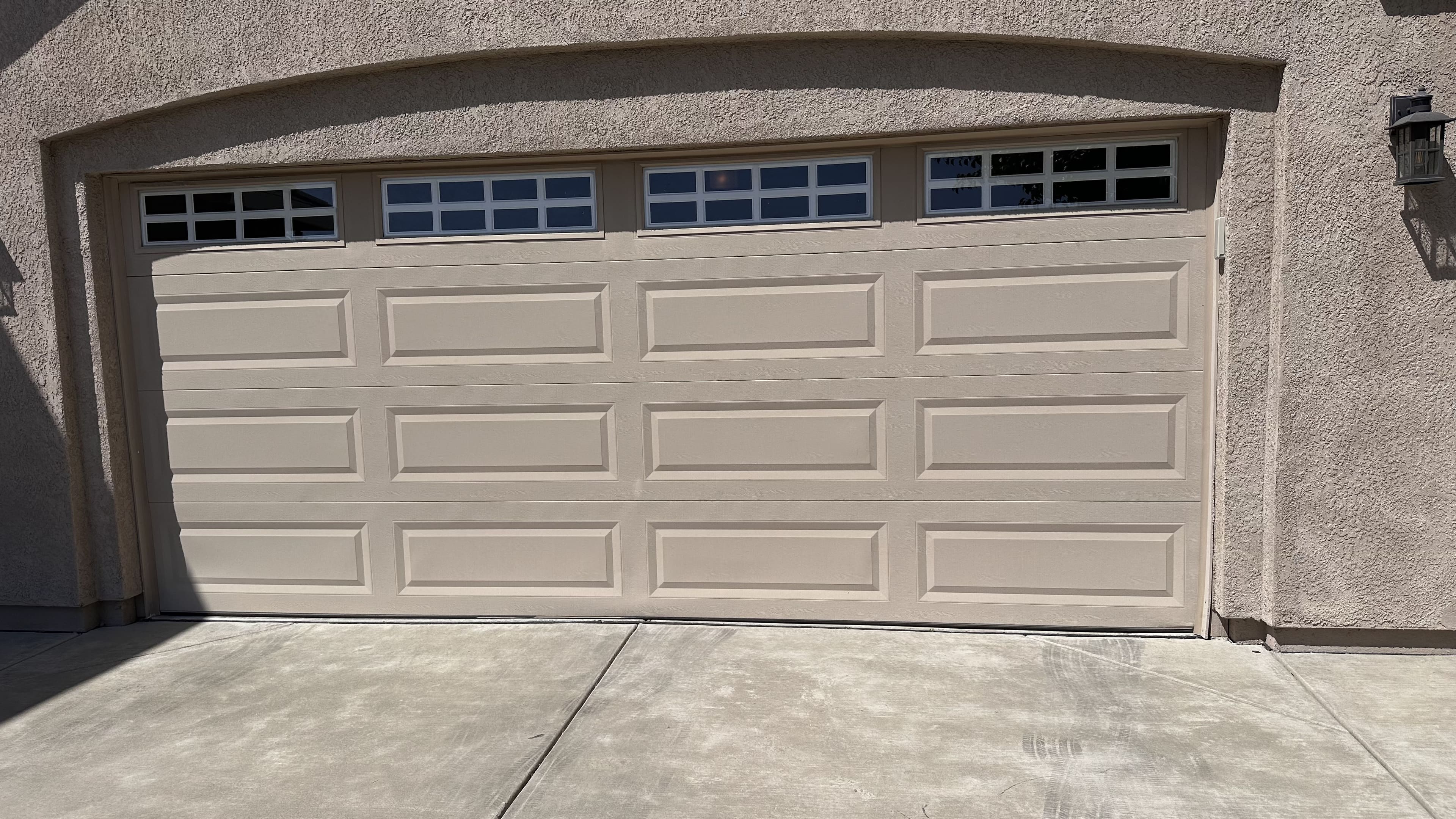 New beige carriage-house garage door with windows installed on a stucco home